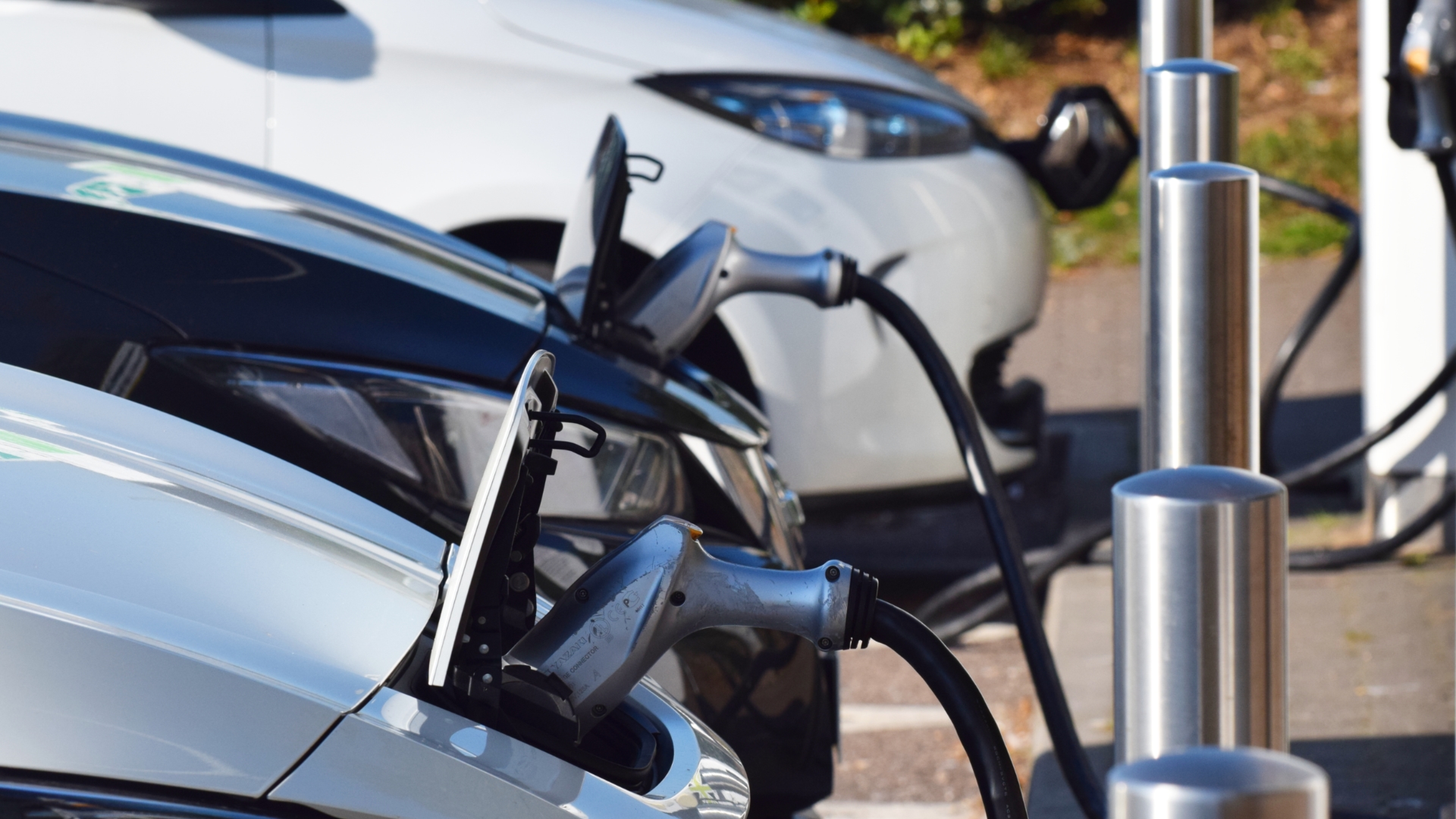 A close up shot of electric vehicles in a line receiving a charge with the cable plugged in