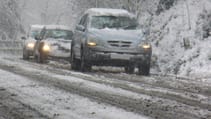 Line of cars driving in snowy conditions on untreated road with treacherous looking conditions