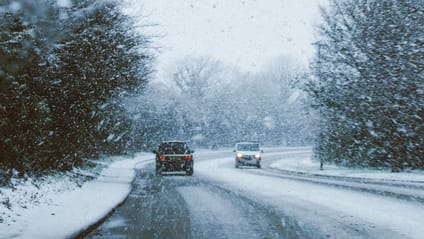 Shot of road bookended by a forest with cars driving in both directions in heavy snow conditions