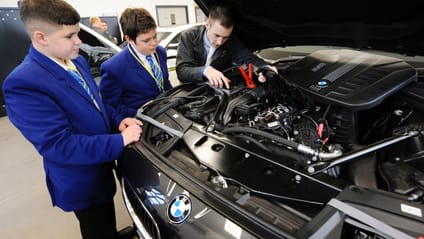 A mechanic shows young students the engine bay of a BMW