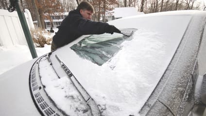 Man scrapes snow and ice from car windscreen, close up shot