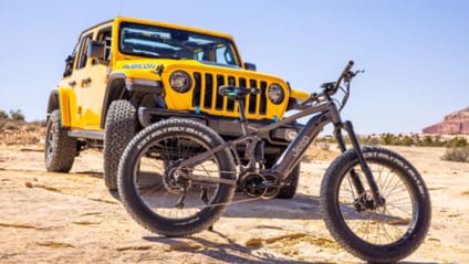 Jeep bike in front of Jeep Rubicon in yellow, both parked on desert surface