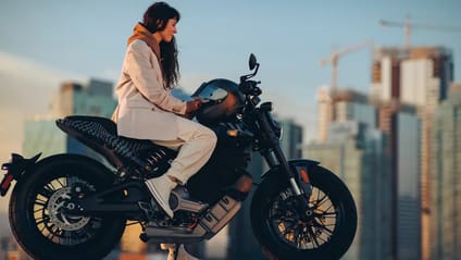 A woman sits astride the LiveWire S2 Del Mar Launch Edition, in profile, with a city skyline backdrop