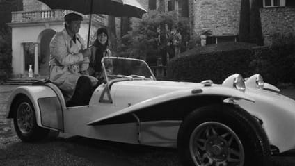 Jean-Paul Belmondo sitting with woman in Caterham Super Seven holding umbrella - black and white shot