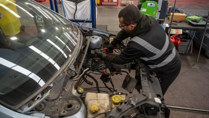 Recycling worker removing electrical wiring from engine bay