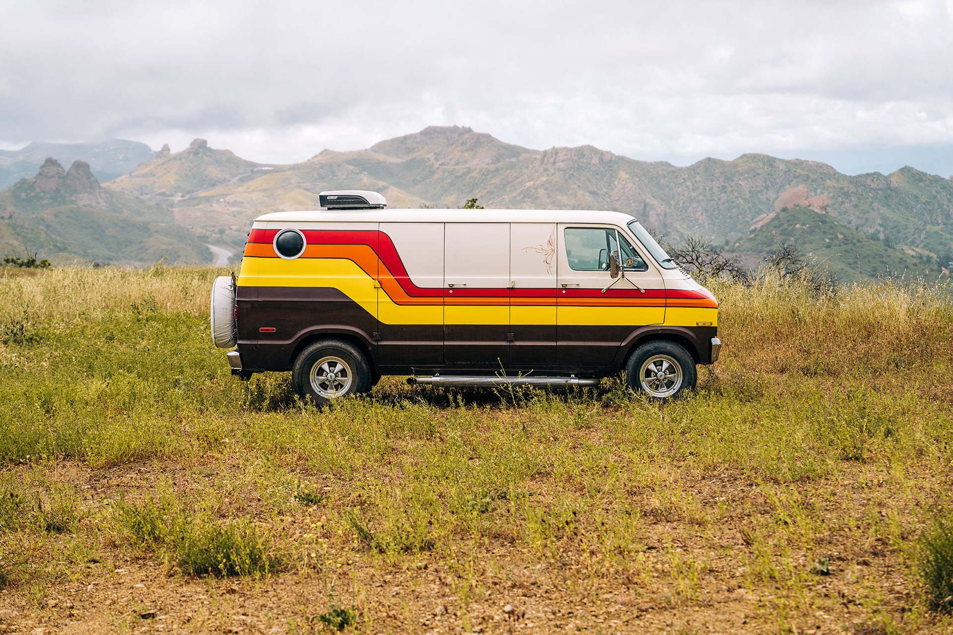 A 1977 Dodge Tradesman camper van side profile shot on grassy meadow