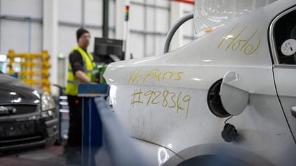 Recycling worker deconstructs car, which has identifying codes written on body panel in yellow chalk pen