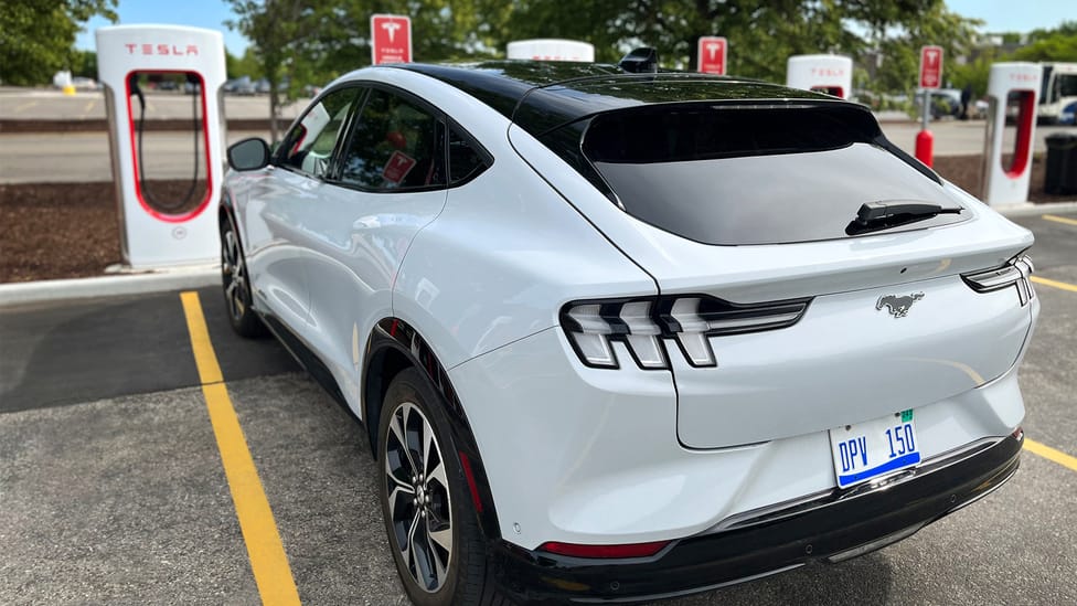 Ford Mustang Mach-E in white parked and charging at a Tesla Supercharger in the US