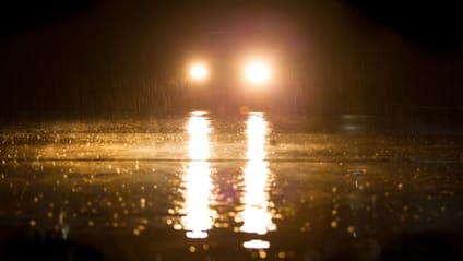 Car in the dark with headlight on, reflecting in a puddle on the road