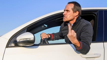 A man hanging out of a car window flashing a middle finger, which has been pixellated