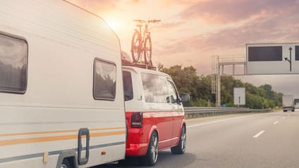 VW camper towing a caravan on motorway in left lane with gantry in background