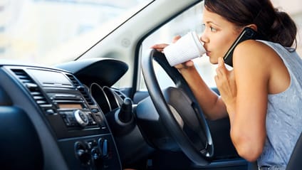 Woman driver eating and cradling phone on shoulder