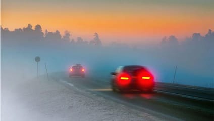 Red brake lights glowing in a car driving away from the lens at dusk