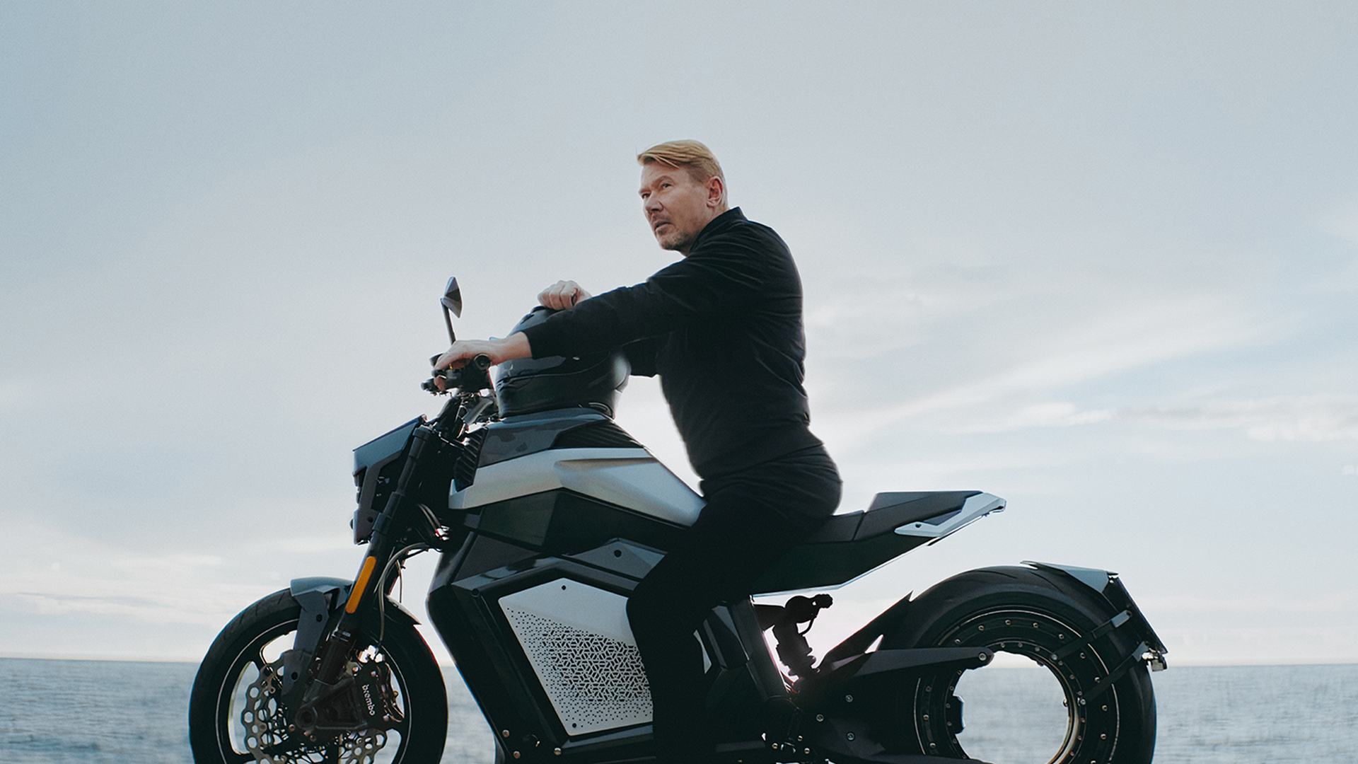 Mika Hakkinen sitting on Verge TS Pro with ocean backdrop