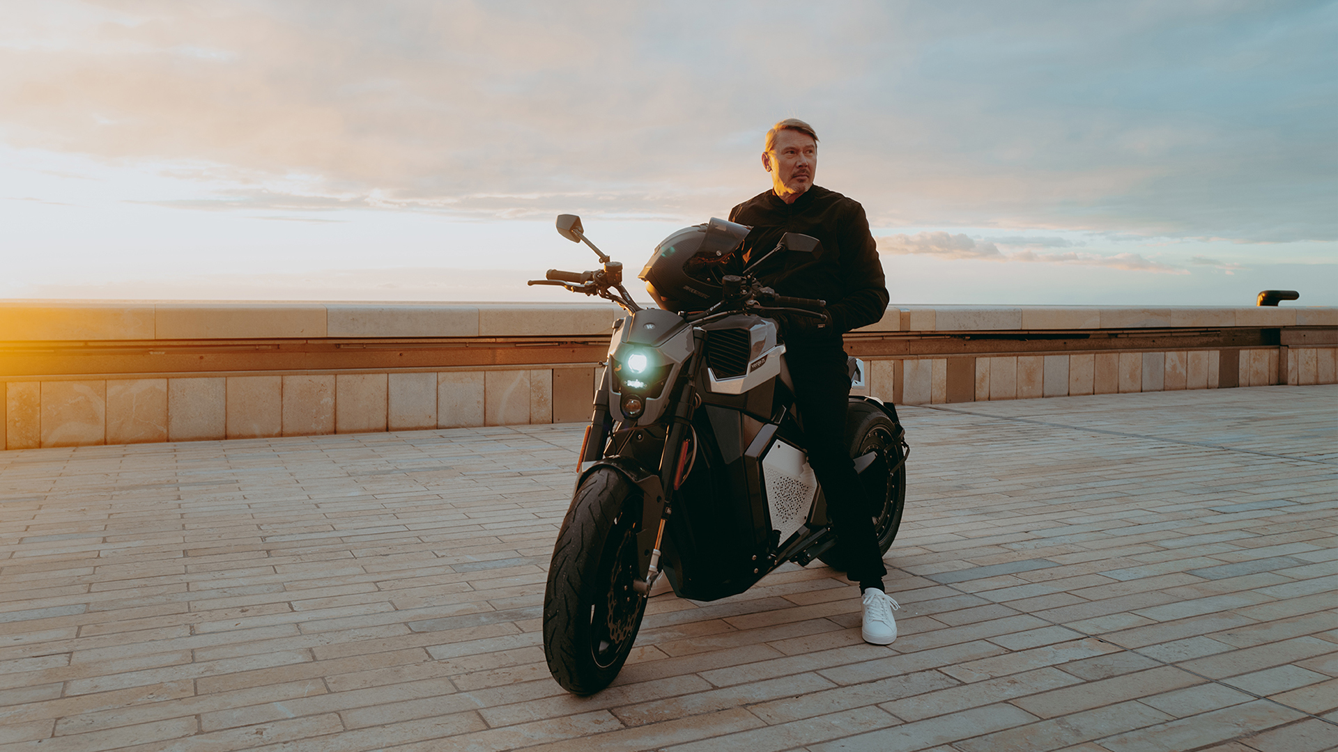 Mika Hakkinen sitting on Verge TS Pro with sunrise backdrop