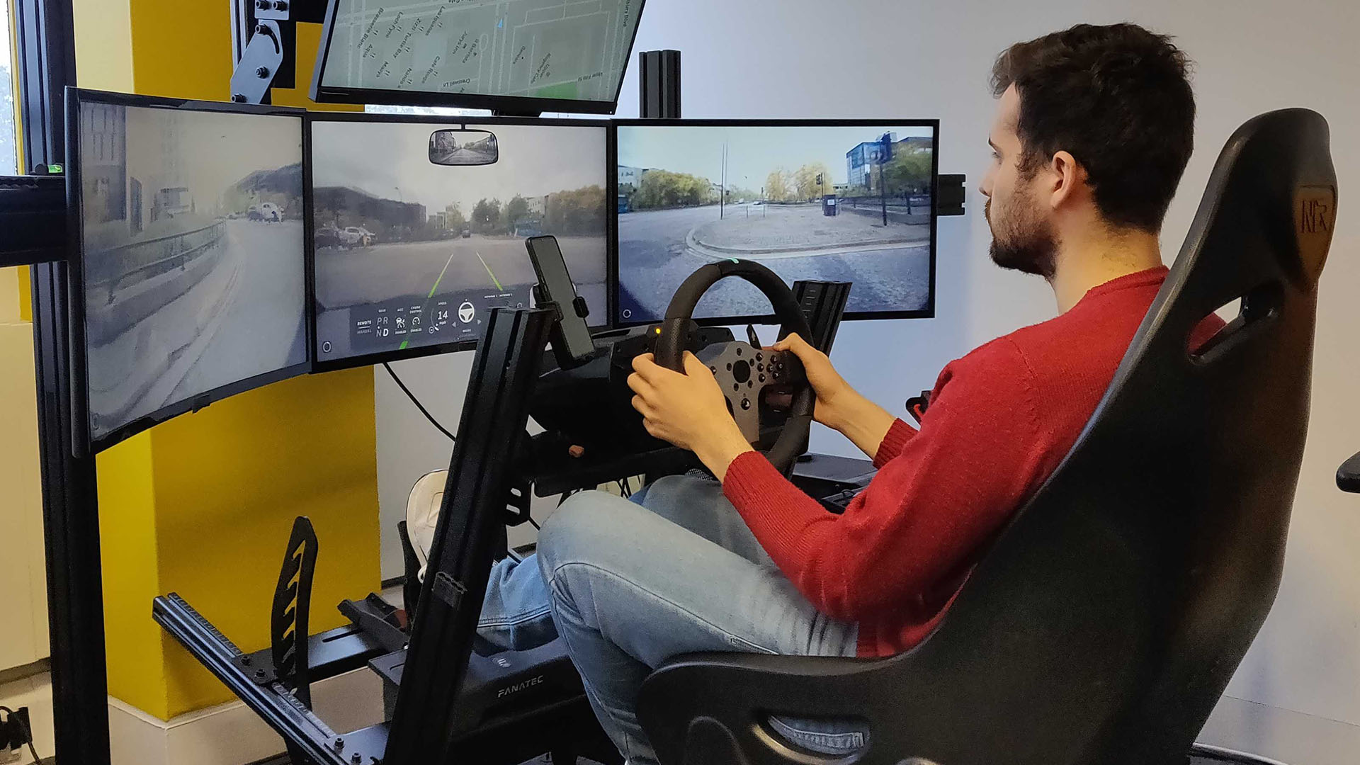 Man sits driving at a console with several monitors