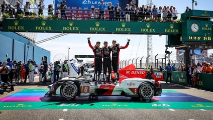 Toyota Gazoo Racing team celebrating fifth win standing on Le Mans winning car under pit bridge with arms in the air