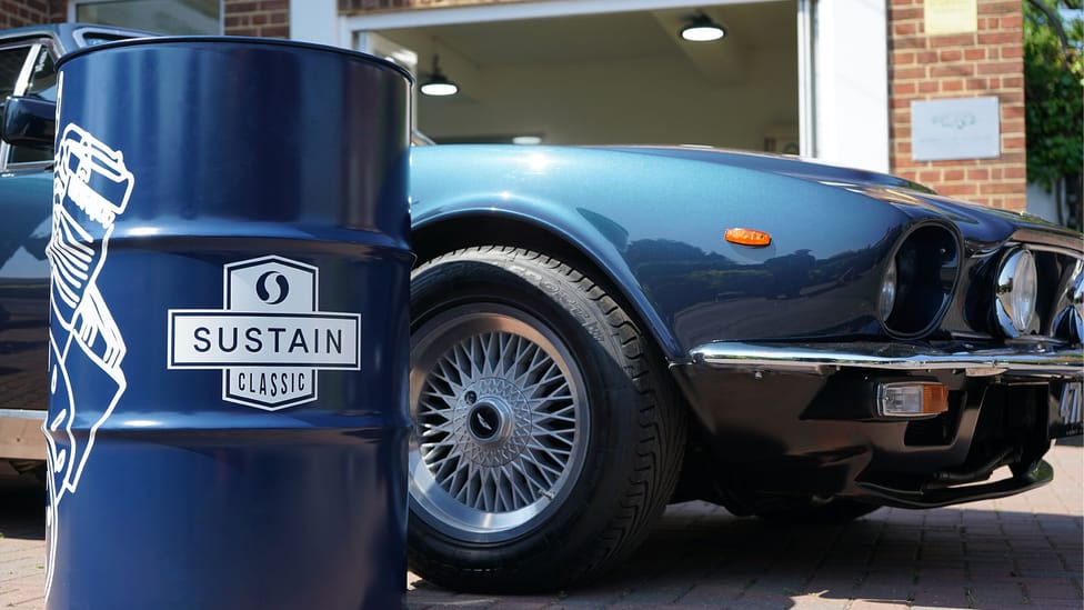 Drum of fuel with Sustain logo on sits in front of classic car - close up shot near wheel