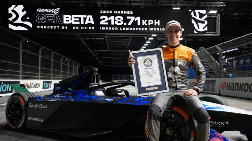 Driver Jake Hughes sits on Genbeta Formula E car under gantry showing world record