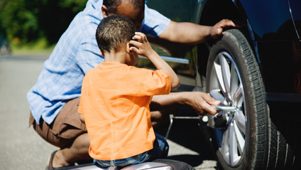 A man changing a tyre with a child next to him