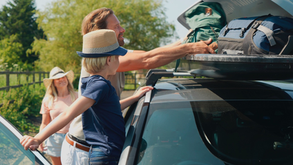 A man grabbing a bag from a roof rack with a woman and child nearby