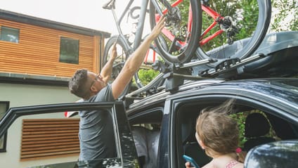 Someone placing a bicycle on a bike carrier on top of a car