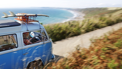 A campervan being driven down a road near the coast 