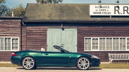 2006 Jaguar XK in front of an old-style garage with the top down