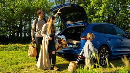 A family of three unpacking outdoor equipment from the boot of a Škoda Enyaq SUV