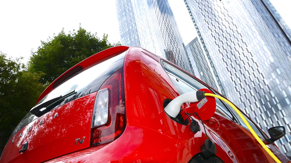 Red Skoda Citing connected to a charger, shot taken from a low angle to get skyscraper in background in frame