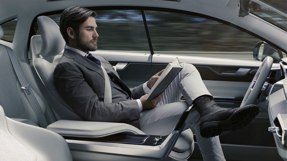 Man sitting in Volvo concept reading a book behind the wheel, demonstrating self-driving vehicle tech