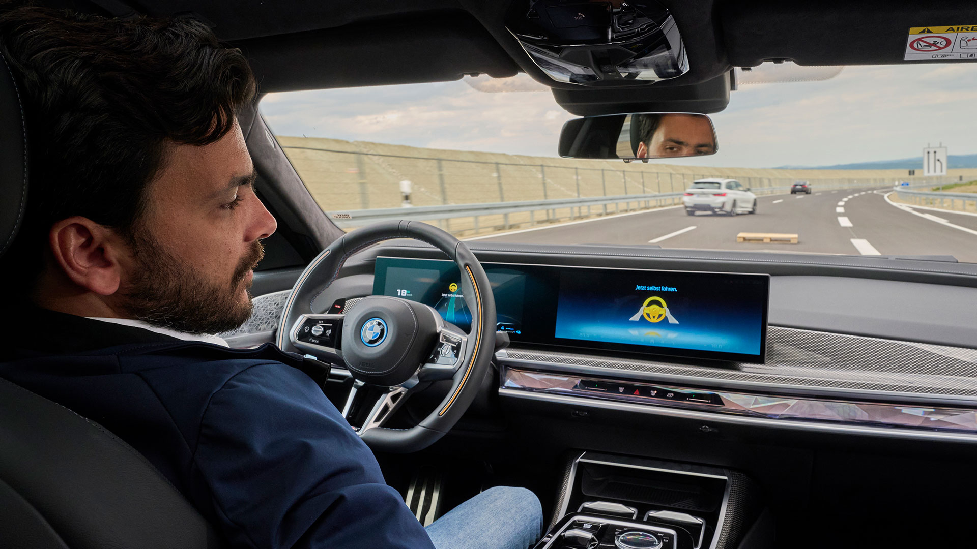 Man sitting in a new BMW 7 Series, behind wheel with hands on knees watching movie on centre screen