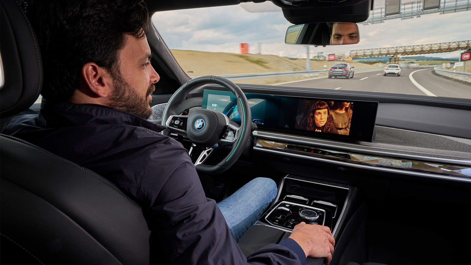 Interior shot looking over driver's shoulder, showing man focussed on centre display while car self-driving on motorway