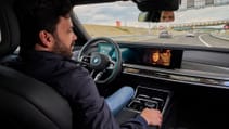 Interior shot looking over driver's shoulder, showing man focussed on centre display while car self-driving on motorway