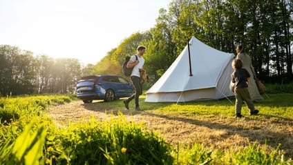 A family on a camping trip stood next to their tent and Škoda Enyaq 85 Edition