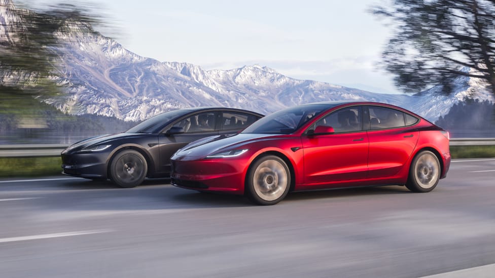 Two updated Tesla Model 3 driving side by side, one in grey, one in red, with mountain backdrop