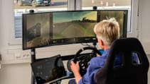 Man sitting at static driving rig with three screens, remotely piloting car around test track