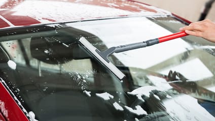 Someone cleaning a car windscreen with a windscreen scraper with sponge & telescopic handle