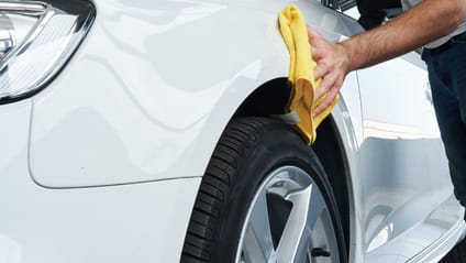 Someone using a cloth to wipe just above the wheel drum of a car 