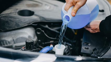 Someone pouring antifreeze into their car's engine cooling system