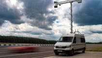 Van parked on roadside with camera rig arched over it, car passing blurred out by speed