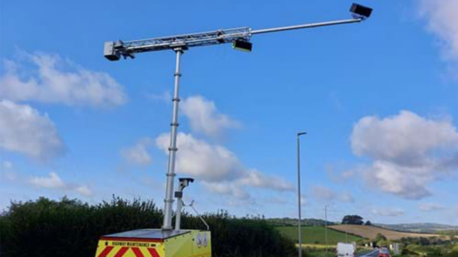 Van parked on roadside with camera rig arched over it, against bright blue sky