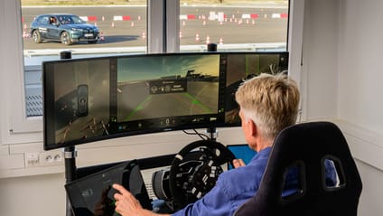 Man sat at a simulator control, with a remote car full-sized in the background navigating cones