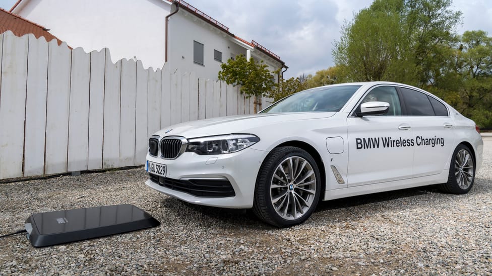 BMW parked in front of a wireless charging pad sitting on the gravel. BMW has 'wireless charging' decals