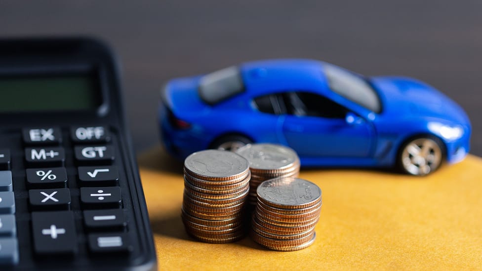 Close up of a pile of coins, a calculator and a blue model car to depict motoring costs