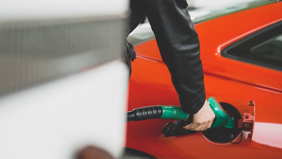 Man using a unleaded pump to refuel red car