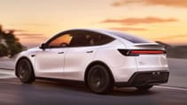 The updated Tesla Model Y driving down a road with a sunset backdrop