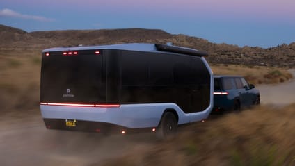 Rear driving shot of the Pebble Flow production EV hitched to an SUV in the desert at dusk