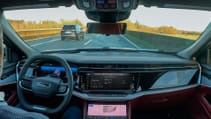 Interior shot of a self-driving car, showing driver with no hands on the wheel or eyes on the road