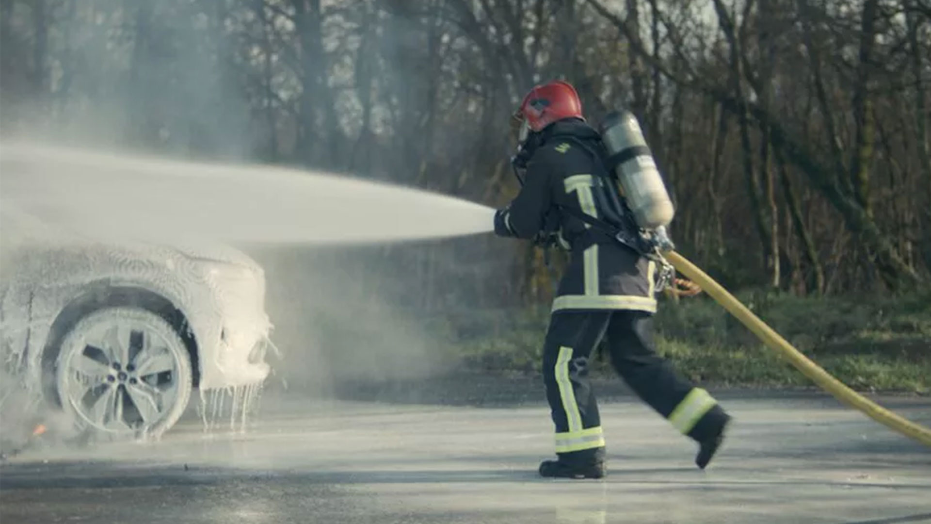 Firefighter using hose to douse front end of vehicle in fire-subduing foam